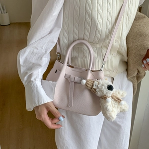 Detailed view of woven texture shoulder bag with cute teddy bear charm on model