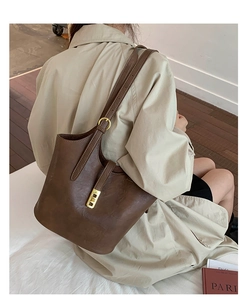 Detail of dark brown bucket bag featuring gold square buckle and pebbled leather texture