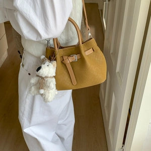 Detail of yellow woven bucket bag with leather handle and white plush bear charm