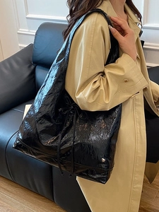 Large black glossy tote bag with heart metal logo worn by a model in a trench coat