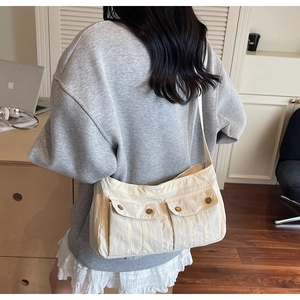 Detail of off-white canvas shoulder bag featuring double front flap pockets with gold buckles