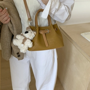 Detail of tan woven bucket bag featuring adjustable strap and plush bear charm