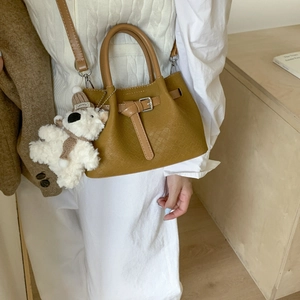 Detail of mustard yellow woven bucket bag featuring a cute white plush bear charm accessory