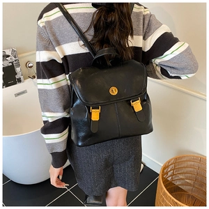 Detailed close-up of a vintage black leather backpack featuring a round gold metal lock