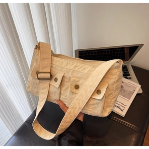 Detailed view of the off-white canvas messenger bag featuring dual front flap utility pockets