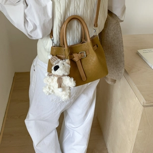Detail of brown woven bucket bag featuring a belt buckle and cute plush bear charm