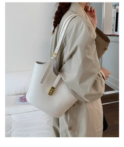 Detail of embossed beige bucket bag with gold hardware worn with a trench coat