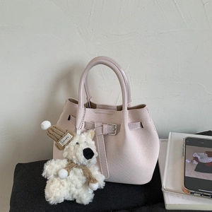 Detail of light pink woven bucket bag featuring decorative buckle and plush bear charm