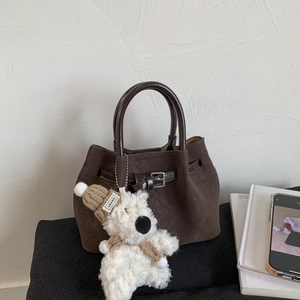 Detail of dark brown woven texture handbag with silver buckle and plush bear pendant