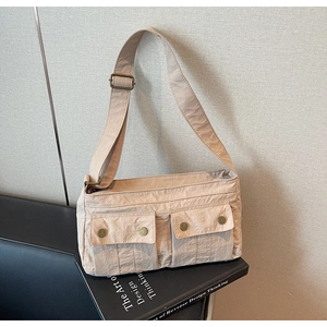 Close-up of beige nylon shoulder bag featuring dual front cargo pockets and metal buttons
