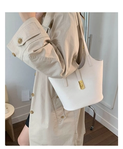 Detailed view of large white leather bucket bag with gold buckle on a beige trench coat