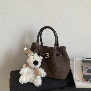 Detail of dark brown woven texture bucket bag with a cute plush bear charm accessory