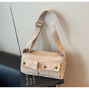 Detail of beige nylon crossbody bag featuring front utility flap pockets and metal snaps