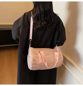 Pink quilted duffel bag on model's shoulder showing crossbody strap and side pocket