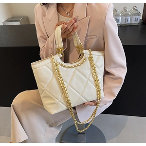 Detailed view of a white quilted tote bag with golden chain strap and large diamond pattern