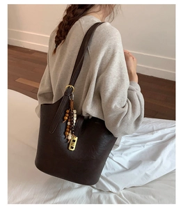 Dark brown leather bucket bag with beaded tassel charm on a model's shoulder