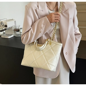 White quilted tote bag with gold chain strap shown on model in light pink blazer