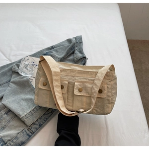 Detailed shot of beige shoulder bag showing front utility pockets and gold metal buckles