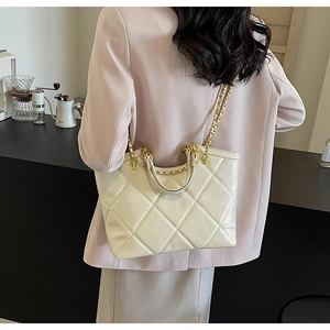 Detail of creamy white quilted tote bag with gold chain strap on a modern background