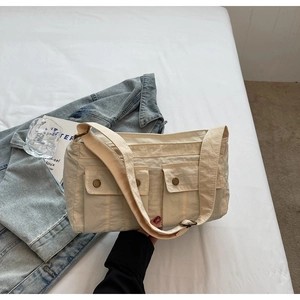 Detail view of beige nylon crossbody bag featuring double front pockets and metal snaps