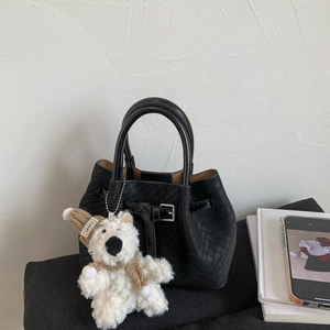Detail of black woven texture shoulder bag featuring a silver buckle and plush bear charm