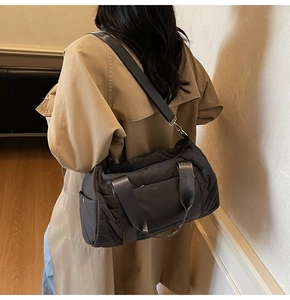 Deep grey quilted nylon bag worn over the shoulder with a stylish beige trench coat