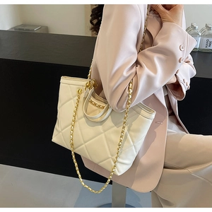 Detail of a beige quilted tote bag with gold chain strap worn by a woman in a pink suit