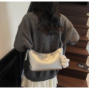 Detail of silver hobo bag with pleated texture and white plush pendant worn by model