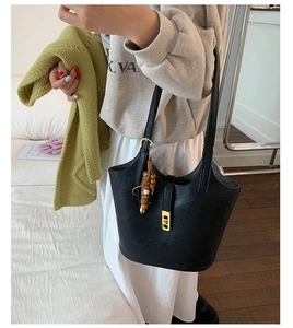 Detail of black leather bucket bag with gold clasp and wooden bead charm on shoulder