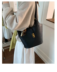 Detail view of black faux leather bucket bag with gold lock and decorative wood beads