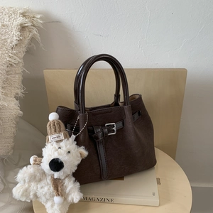 Deep brown textured bucket bag with retro buckle and cute teddy bear charm on wood stool