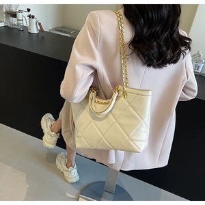 Detail of a beige quilted tote bag with gold chain strap and quilted faux leather texture