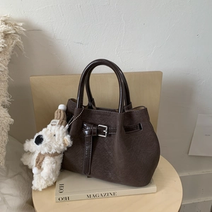 Detail of dark brown woven textured bucket bag with teddy bear charm on a magazine