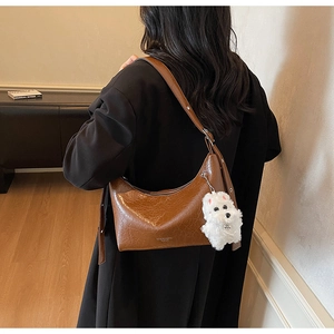 Detail of brown faux leather hobo bag with a cute white plush puppy charm and adjustable strap