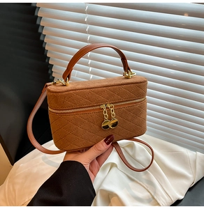 Detail of a brown box-shaped handbag with diamond stitching and golden metal hardware