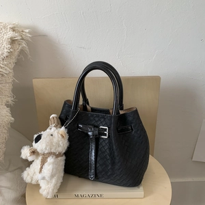 Close-up of black woven leather bucket bag with silver buckle and cute teddy bear charm