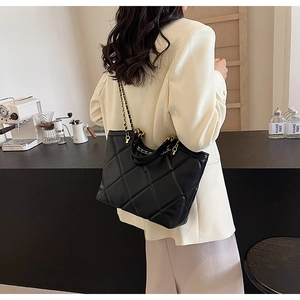 Quilted black tote bag with chain strap worn over a beige blazer in a cafe