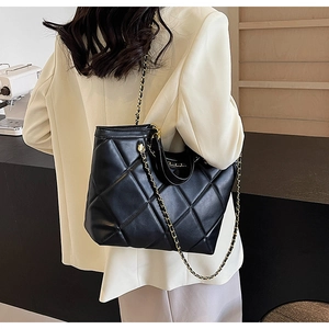 Detail of black quilted leather tote bag with metal chain strap on model's shoulder