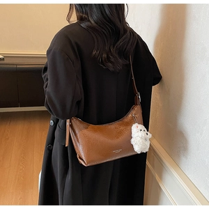 Brown oil wax leather hobo shoulder bag with plush pendant on a black coat back view