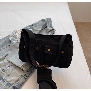 Detail of black canvas shoulder bag featuring multiple flap pockets and bronze metal buttons
