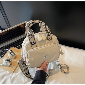 Detail der cremeweißen Umhängetasche mit Markenriemen neben einem Laptop und Kopfhörern