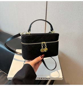 Detail of black quilted suede box bag with gold metal hardware on a white book base