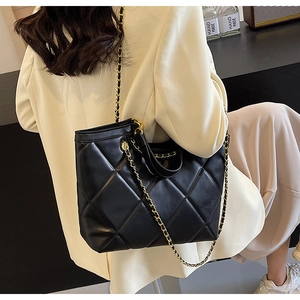 Detail of black quilted tote bag featuring golden chain straps and elegant leather texture