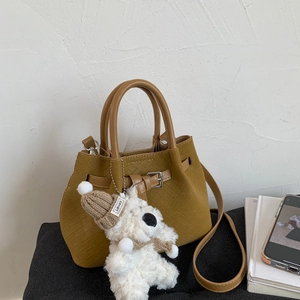 Detail of ginger yellow woven bucket bag with a cute plush dog charm on a soft cushion