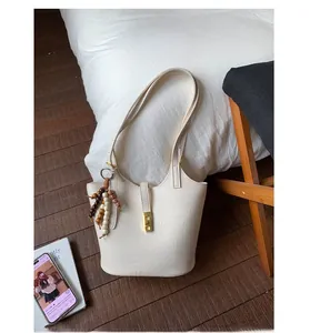 Detail of white leather bucket bag with gold buckle and beaded charm in home setting