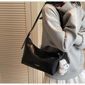 Detail of black glossy faux leather shoulder bag with plush puppy charm on a model