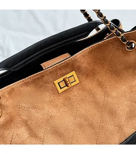 Close-up of golden metal twist lock on a brown suede tote with diamond stitching