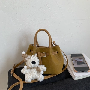 Detail of yellow woven bucket bag with long shoulder strap and cute plush bear charm