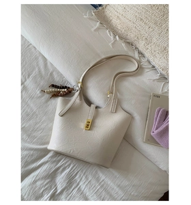 Close-up of cream leather tote bag with golden twist lock and colorful beaded charm