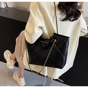 Close-up of black quilted tote bag with golden chain straps on white suit